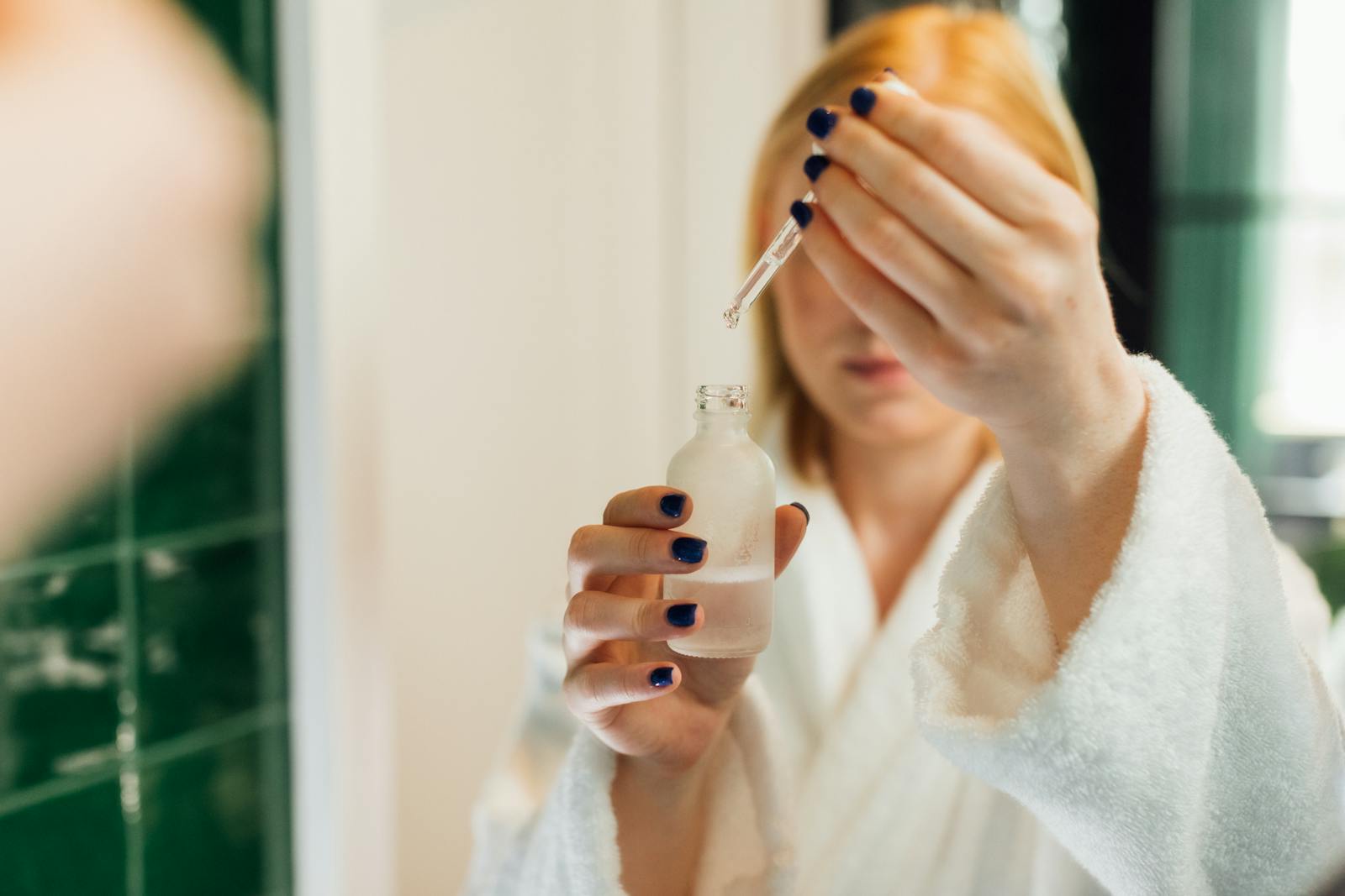 Femeie ținând o sticlă de ser cu Hyaluronic Acid în fața unei oglinzi de baie