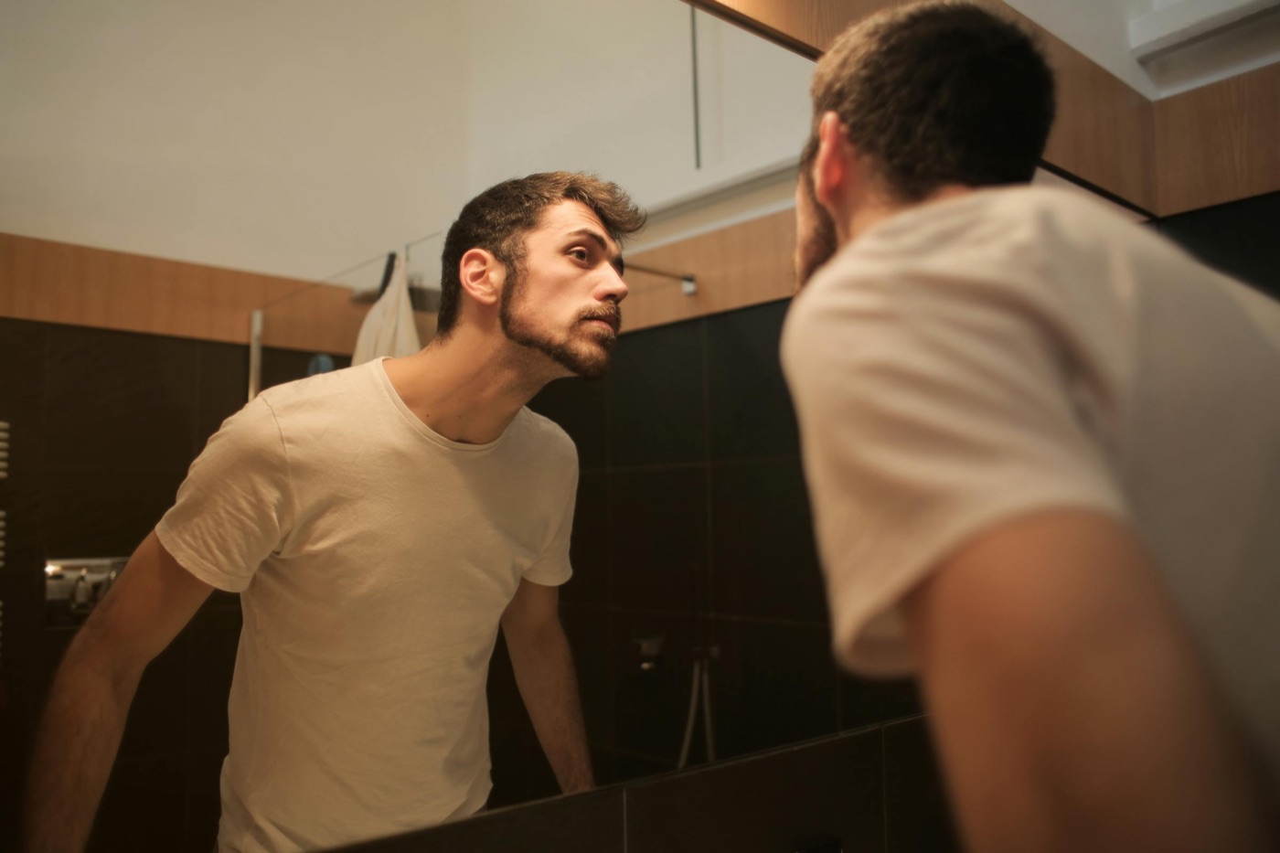 Young man applying skincare in front of bathroom mirror representing men's grooming and skincare routine