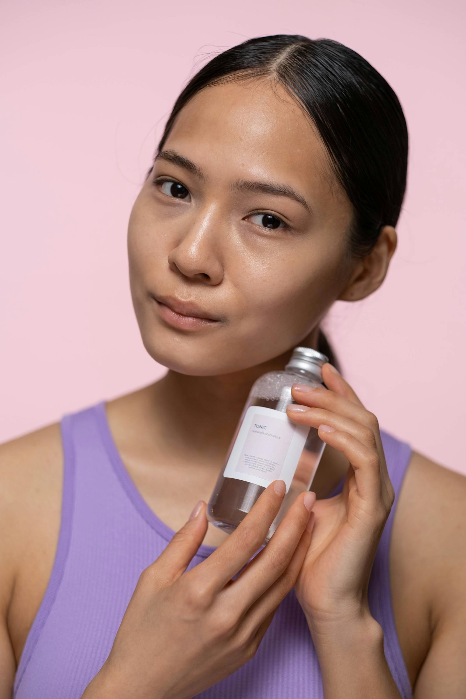 Femeie ținând o sticlă cu esență de mucină de melc pe un fundal pastel moale, formatul K-Beauty care a popularizat ingredientul
